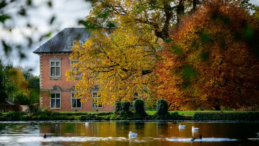 House with a lake in front and autumn trees to right